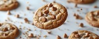 Freshly baked chocolate chip cookies with melting chunks floating against white background, showcasing golden brown texture and scattered crumbs.