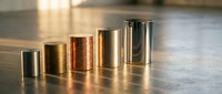 Metallic cylinders in varying sizes arranged in ascending order on concrete surface, showcasing gold and bronze finishes for product display and industrial design concepts.