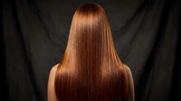 Back view of a woman with long, straight, glossy auburn hair against a dark background, showcasing healthy shine and smooth texture.