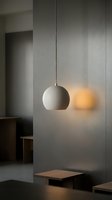 Minimalist pendant lamp with spherical white shade hanging from chain above wooden platform in modern interior space with neutral tones and soft ambient lighting.