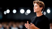 Young confident businessman giving presentation on stage with spotlights in background, professional speaker at corporate event or conference.