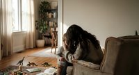 Young woman with long dark hair sitting on couch looking stressed or overwhelmed in cozy living room with natural light for mental health concepts.