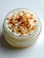 Creamy dessert in glass jar topped with caramelized sugar crumbs, resembling crème brûlée or rice pudding on white background.