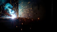 Industrial welding process with bright electric arc and flying sparks against dark background for manufacturing and metalwork projects.