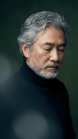 Mature Asian man with gray hair and beard in contemplative pose wearing black turtleneck against dark background for portrait photography and lifestyle content.