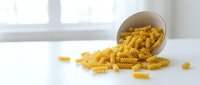 Uncooked fusilli pasta spilling from a white bowl onto a bright surface, ideal for food and cooking content.