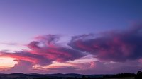 Dramatic purple and pink sunset sky with vibrant clouds over mountain silhouettes creating stunning twilight atmosphere for nature backgrounds.
