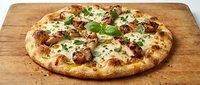 Freshly baked pizza with melted cheese, meat toppings and fresh basil on wooden board, ready to serve for lunch or dinner.