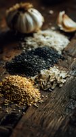 Assorted cooking ingredients with garlic bulb, black sesame, white rice, fennel seeds, and golden flaxseed arranged on rustic wooden surface for culinary use.