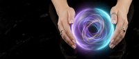 Female hands cupping glowing purple and blue energy orb with swirling light patterns on dark marble surface for spiritual healing and meditation concepts.