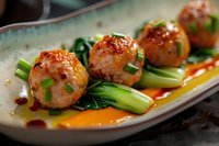 Glazed Asian meatballs served with baby bok choy in sweet chili sauce on ceramic plate, close up view of appetizer with garnished green onions.