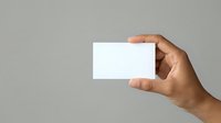 Hand holding blank white business card against neutral gray background, suitable for branding, corporate identity, and marketing mockup designs.