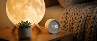 Cozy bedroom nightstand with glowing moon lamp, digital alarm clock, and succulent plant creating warm ambient lighting for relaxation and sleep.