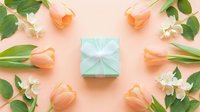 Mint gift box with white ribbon surrounded by peach tulips and jasmine flowers on pastel pink background, flat lay for spring holiday greeting.
