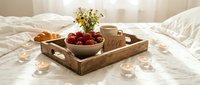 Romantic breakfast in bed on wooden tray with strawberries, croissant, coffee cup, wildflowers, and candles on white linen.