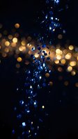 Blue glitter particles falling with golden bokeh lights on dark background creating magical sparkle effect for celebration and party designs.