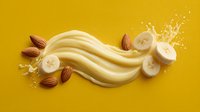 Creamy banana almond smoothie splash with flowing waves on yellow background. Fresh fruit and nuts for healthy breakfast drinks and nutrition concepts.