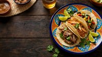 Authentic street tacos with seasoned meat, fresh cilantro, and lime wedges served on decorative plate with rustic wooden table setting for food photography.
