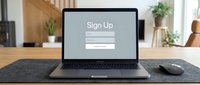 Laptop on wooden desk displaying a sign up registration form screen, modern home office background, online account creation concept.