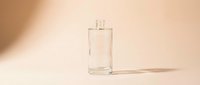 Clear glass perfume bottle with minimalist design on neutral beige background, casting soft shadow, suitable for cosmetics, fragrance, and beauty product marketing.