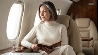 Elegant businesswoman reading book in luxury private jet cabin during flight, professional travel and executive lifestyle concept.