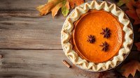 Fresh baked pumpkin pie with fluted crust and star anise garnish on rustic wooden background with autumn maple leaves, overhead view for seasonal baking.