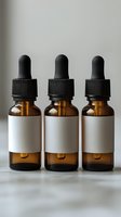 Three amber glass dropper bottles with blank white labels and black caps arranged in row on light surface. Essential oil or medicine packaging mockup.