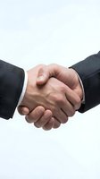 Two businessmen in dark suits shaking hands against a light background, symbolizing partnership, agreement, and professional trust.