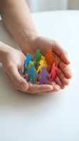 Cupped hands holding colorful paper cutout figures in circle representing community support, teamwork, diversity and social connection concepts.