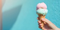 Hand holding waffle cone with pink and mint ice cream scoops against vibrant turquoise wall, perfect for summer refreshment advertising.