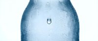 Close-up of water droplet forming horseshoe shape on frosted blue bottle surface against white background, representing hydration and freshness.