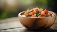 Fresh diced tomatoes with chopped herbs in wooden bowl on rustic table, shallow depth of field with soft natural lighting and blurred background.