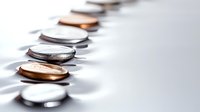 Row of silver and copper coins arranged in line casting shadows on white surface, representing financial concepts and money management.