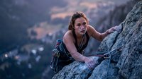 Young athletic woman rock climbing on mountain cliff during sunset with determination and focus for outdoor adventure sports and fitness activities.