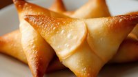 Golden crispy samosas with flaky pastry shells arranged on white plate, traditional Indian appetizer snacks ready for serving at restaurant or home.