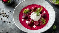 Vibrant beet soup with roasted beets, sour cream dollop, fresh dill garnish and black pepper served in speckled ceramic bowl on dark background.