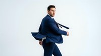 Young adult male, Caucasian, wearing navy business suit and tie, running with dynamic energy and determination against white background for corporate success and career advancement concepts.