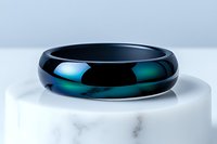 Sleek black ceramic ring with iridescent blue-green finish on white marble surface, showcasing modern minimalist jewelry design for luxury accessories market.