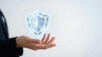 Businessman hand presenting glowing digital security shield symbol for cyber protection and data safety in corporate environment.