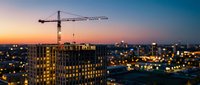 Construction crane building modern residential complex at sunset with city lights and urban development skyline in evening twilight atmosphere.