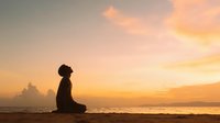 Young woman meditating in lotus position on beach at golden sunset with peaceful ocean waves and dramatic sky for wellness and mindfulness concepts.