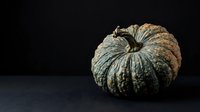 Textured green and tan striped decorative gourd or ornamental squash isolated on dark background, suitable for autumn, fall, and harvest-themed designs.
