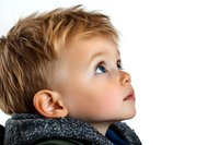 Young caucasian boy with blue eyes looking up with wonder and curiosity while wearing a cozy gray scarf, captured in profile view against white background.