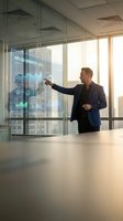 Professional Caucasian businessman in navy suit presenting KPI data analytics on futuristic holographic display in modern glass conference room office.