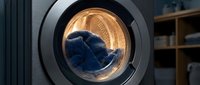 Blue jeans tumbling inside modern washing machine drum during laundry cycle. Household chore and fabric care concept for cleaning advertisements.