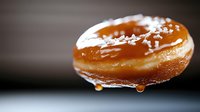 Glazed donut with dripping caramel sauce and sugar crystals on dark background, macro shot showing texture details and sweet reflective coating.