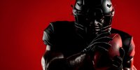 Dramatic portrait of African American football player holding ball against vibrant red background, showcasing strength and determination in professional sports.