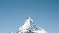 Snow-covered alpine peak with distinctive pyramidal shape against clear blue sky, suitable for travel, nature, and mountain landscape projects.