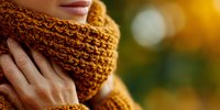 Close-up of woman wearing cozy knitted orange scarf in autumn with blurred golden bokeh background, showcasing seasonal fashion and warmth.
