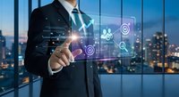 Businessman touching digital interface with glowing icons in modern office overlooking city skyline at dusk. Corporate technology and innovation concept.